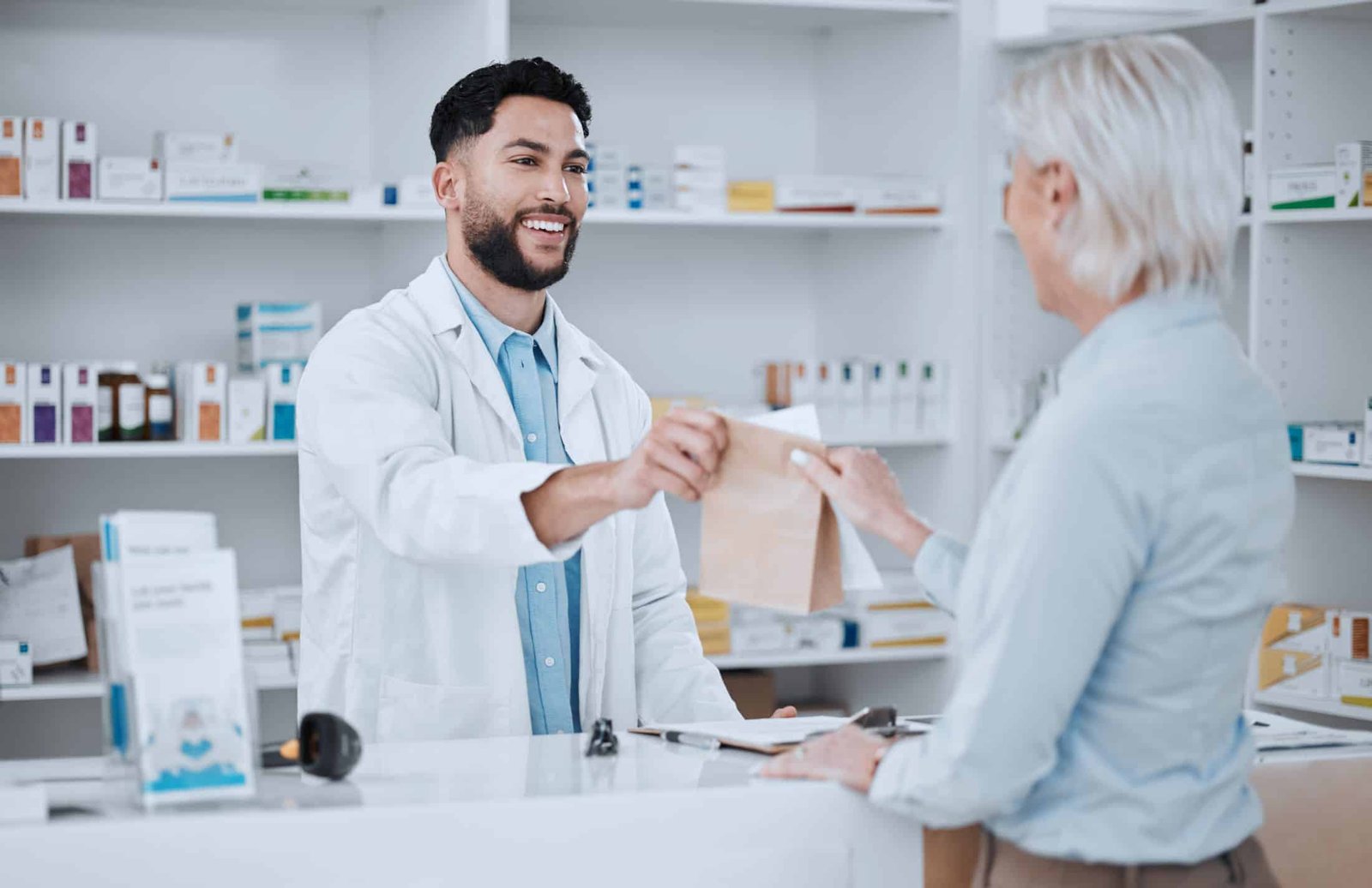 Apotheker übergibt einer Kundin eine Papiertüte mit Arzneimitteln