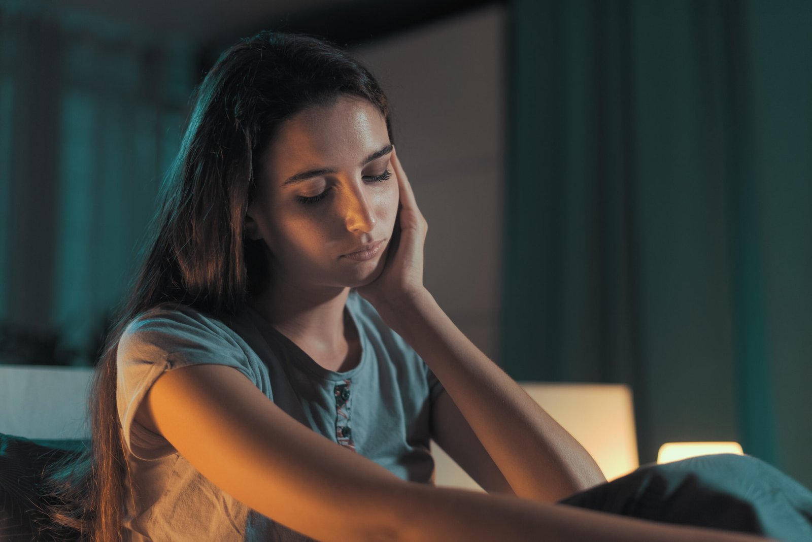 Frau sitzt nachts auf einem Bett und hält sich nachdenklich an die Schläfe
