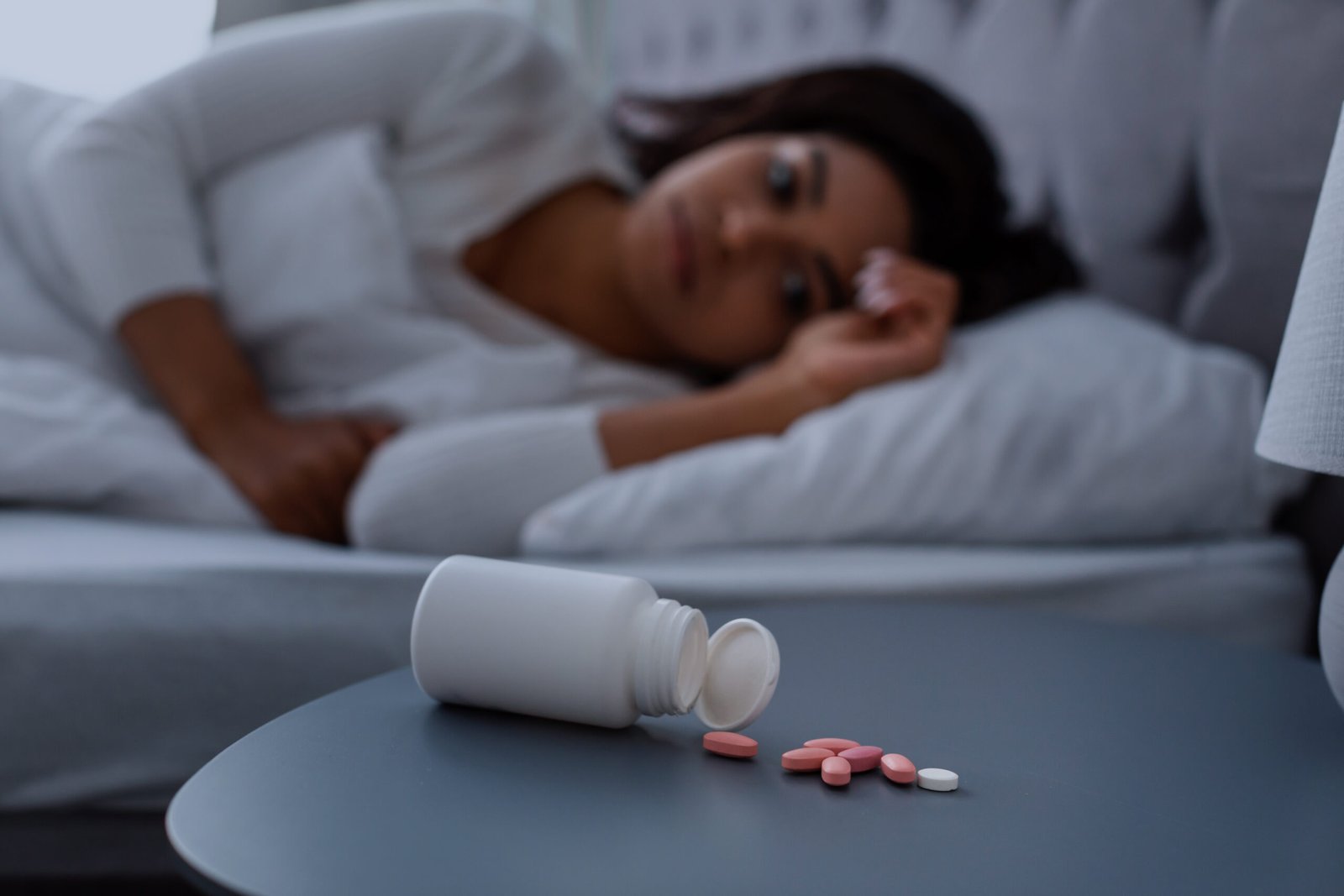 Frau liegt nachts im Bett, während Tabletten neben einer geöffneten Medikamentenflasche liegen