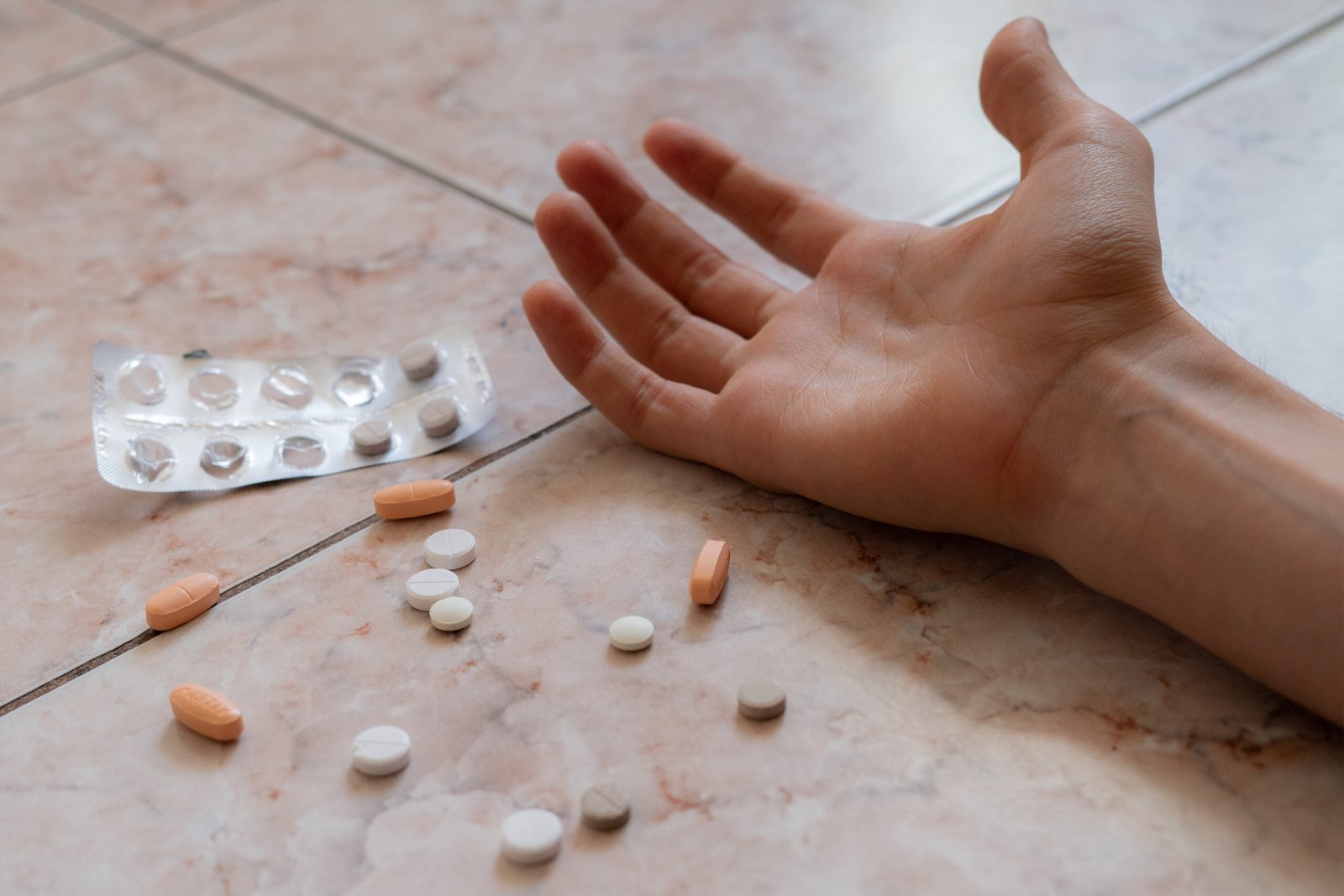 Mehrere Tabletten liegen neben einer ausgestreckten Hand auf dem Boden
