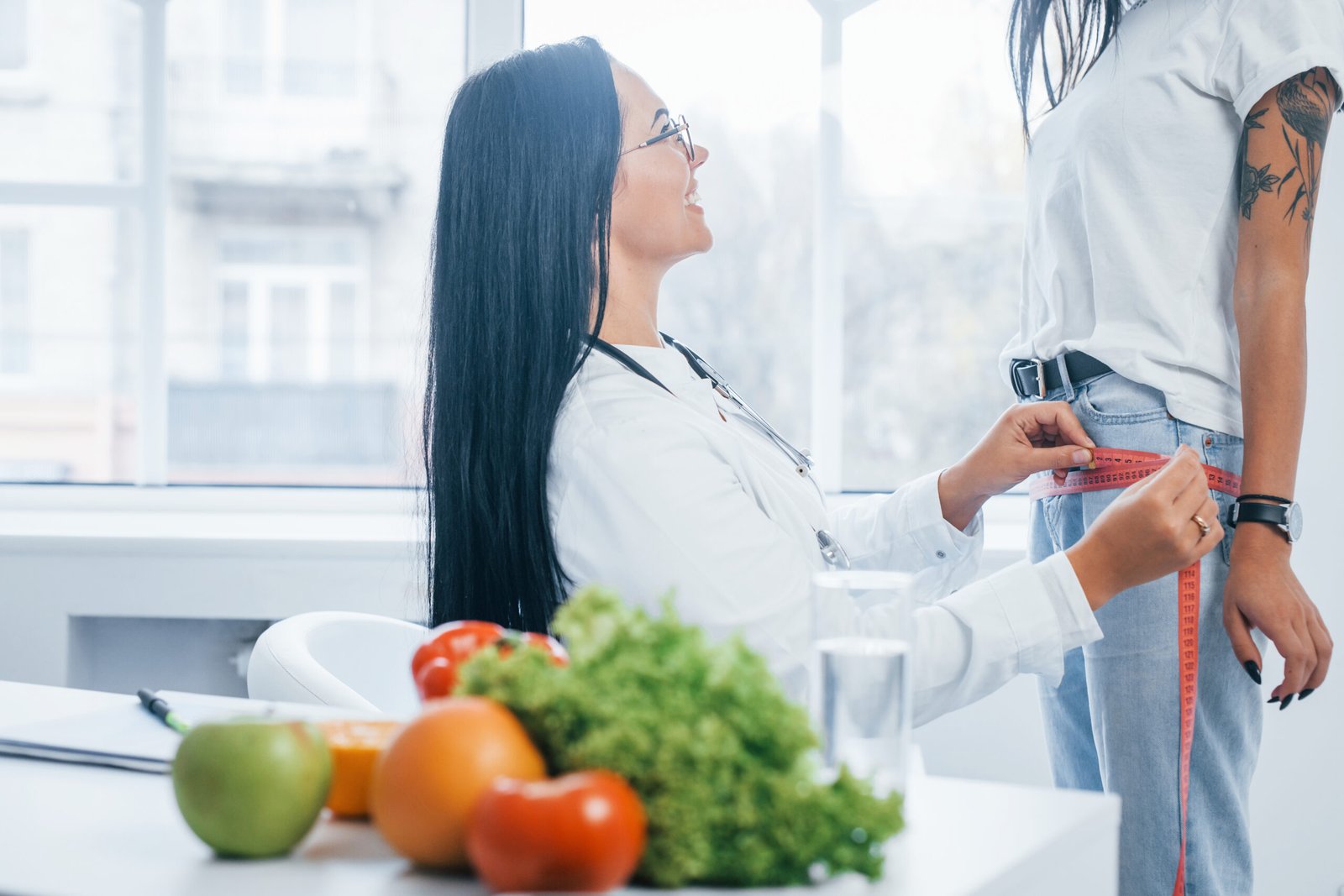 Ärztin misst mit einem Maßband den Taillenumfang einer Patientin