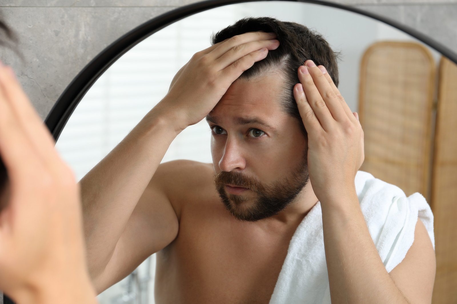 Mann betrachtet seinen Haaransatz im Spiegel und streicht die Haare zurück